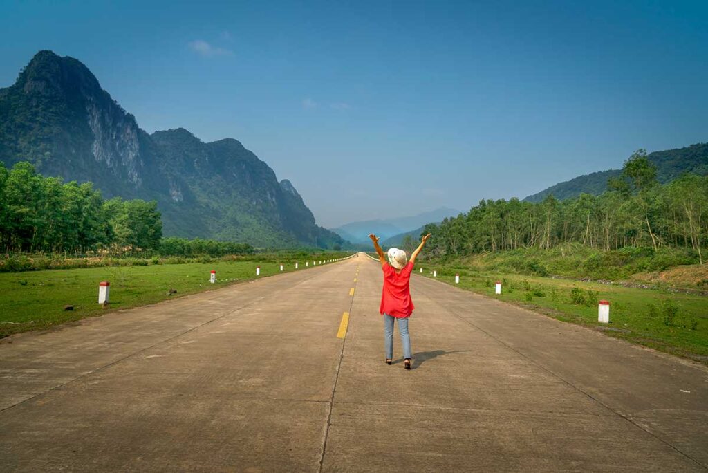 Traveler standing on an empty stretch of the Ho Chi Minh Highway near Phong Nha, with dramatic limestone mountains and wide open scenery