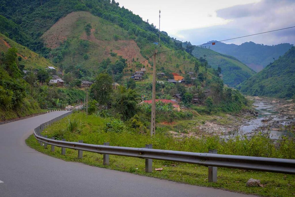 Winding section of the Ho Chi Minh Trail passing a rural village and river valley, showing the scenic countryside of central Vietnam