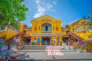 Hoi An Central Market entrance – Yellow colonial-style building of Hoi An Central Market with steps, lanterns, and busy stalls at the entrance.