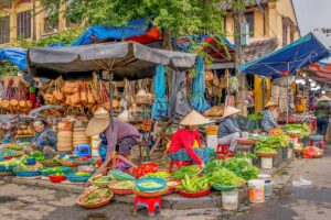 Outdoor stalls at Hoi An Central Market – Street vendors in conical hats selling vegetables and handmade baskets outside Hoi An Central Market in the Old Town.