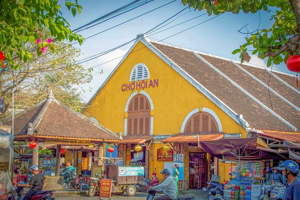 Hoi An Central Market in the Old Town, with its yellow colonial building and bustling stalls selling local food, spices, and souvenirs.