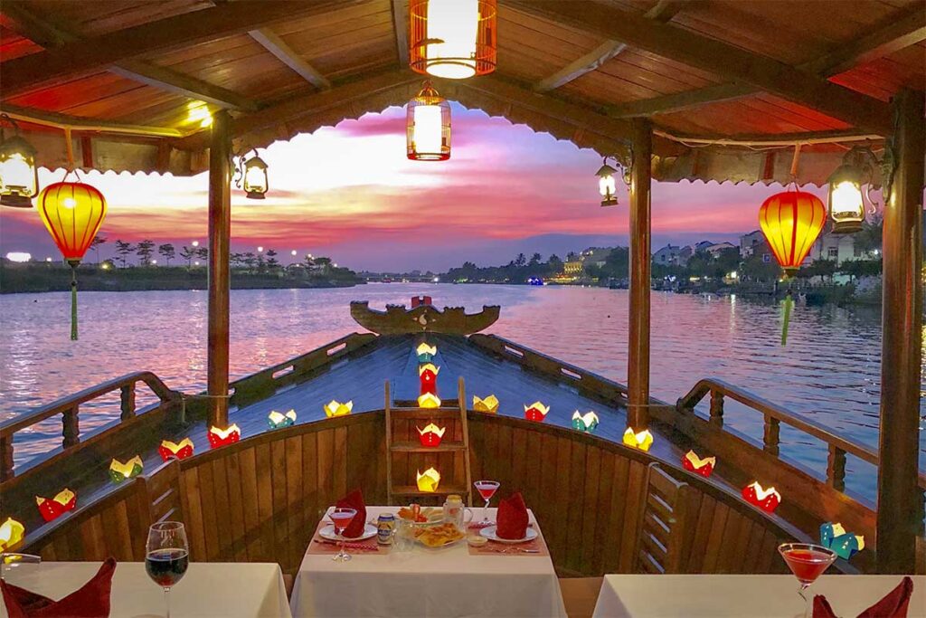 Romantic dinner cruise on the Thu Bon River during sunset – luxury boat ride in Hoi An with lanterns and fine dining setup.