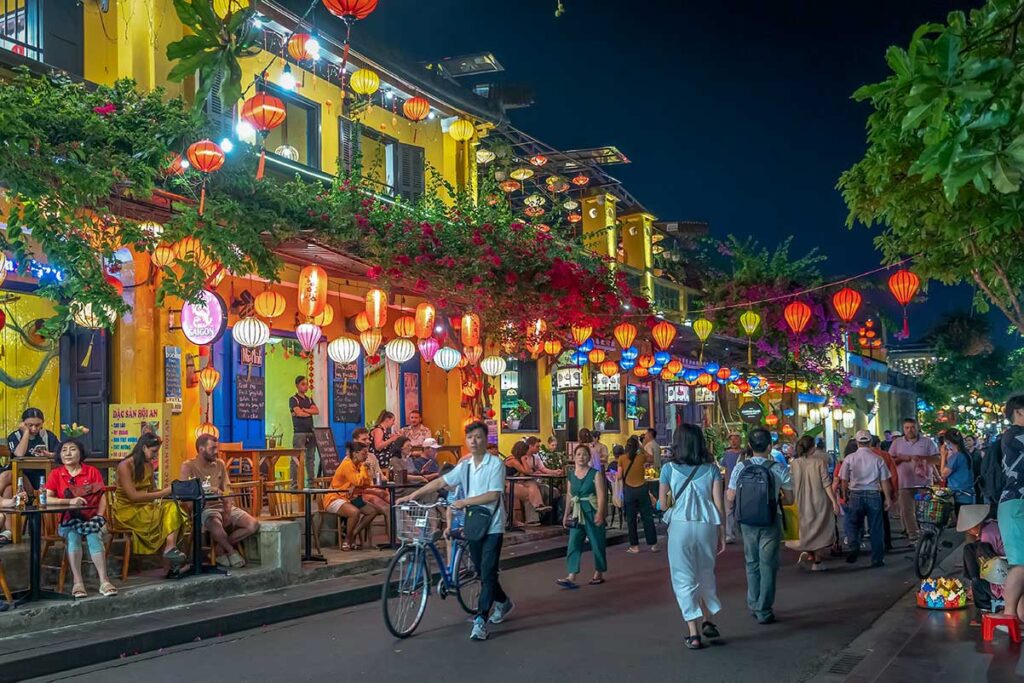 “Colorful lanterns lighting up the streets of Hoi An Ancient Town at night with cafés and people enjoying the lively atmosphere.