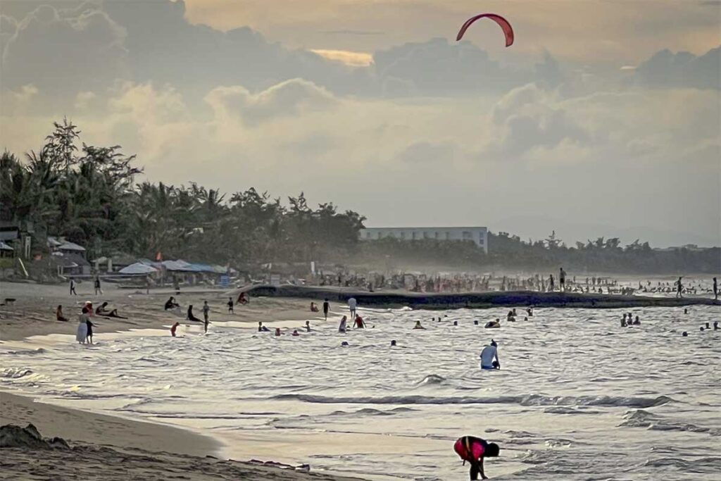 Hoi An Hidden Beach with kitesurfer at sunset – Local beachgoers swimming and relaxing along Hoi An’s Hidden Beach as a colorful kite rises into the evening sky.