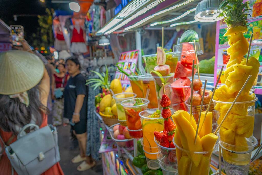 Fresh fruit juice and tropical snacks at Hoi An Night Market, with visitors browsing colorful stalls at night.