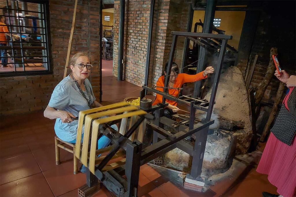 Tourist trying traditional silk reeling techniques alongside local artisans in Hoi An Silk Village.