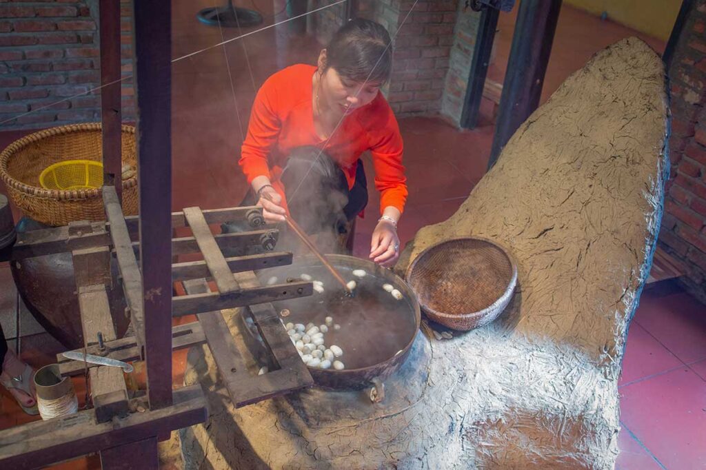 Woman boiling silkworm cocoons to extract silk threads in Hoi An Silk Village.
