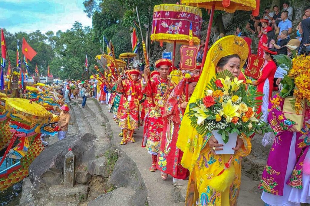 People on traditional clothes from dynasty times walking along the Perfume River next to dragon boats at the Hon Chen Temple for the Hon Chen Festival