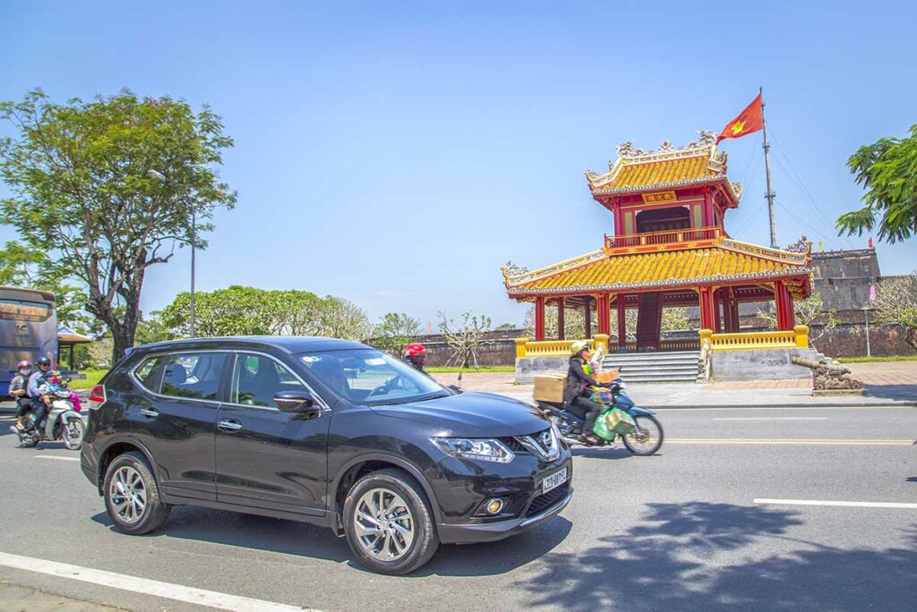 A Hue car rental with driver is passing along a small shrine in Hue