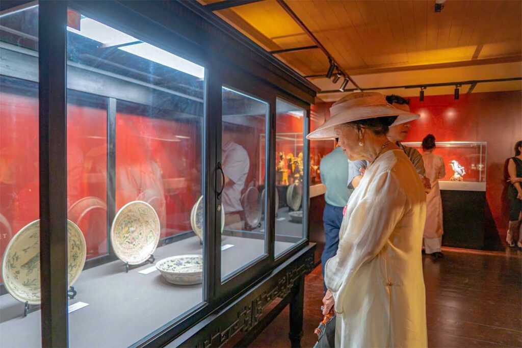 A nicely dressed Vietnamese elderly woman is looking through a glass display in a museum during Hue Festival