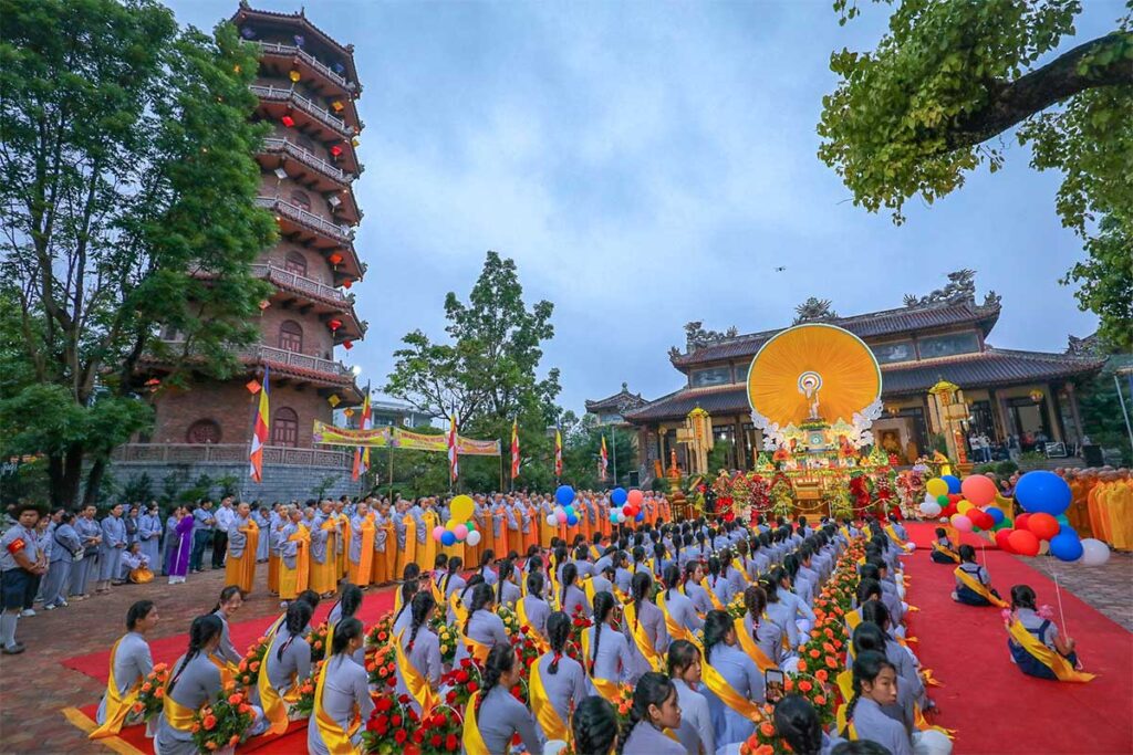 A large gathering of people all wearing grey robes and monks on the side in front of Thien Mu Pagoda during Hue Festival
