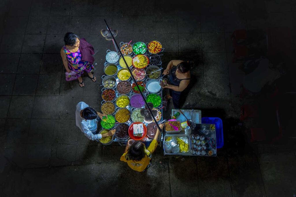 A local street food place in Hue where they sell  Chè Hue – Sweet Dessert Soups. Seen from atop with different colors of each che and toppings
