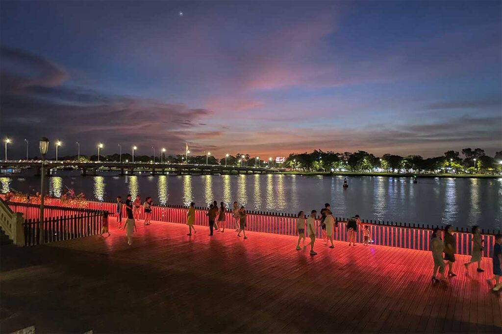 Hue walking promenade along the Perfume River with locals walking along the nicely lid walkway