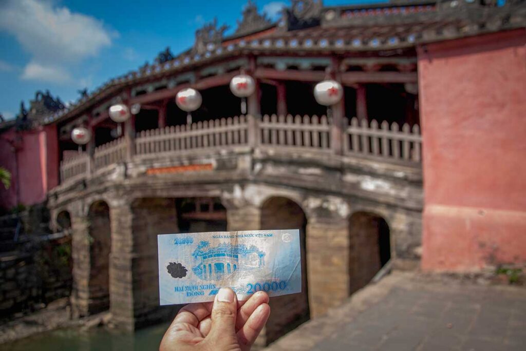 Japanese Covered Bridge Hoi An with 20,000 VND note – traveler holding Vietnamese currency featuring the bridge, highlighting its cultural and historic symbolism.