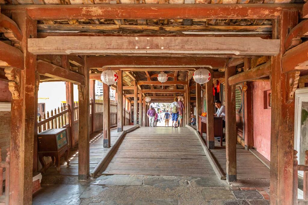 Wooden interior walkway Japanese Bridge Hoi An – The covered passageway of the Japanese Bridge, with timber beams and hanging lanterns guiding visitors through this centuries-old structure.