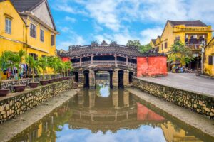 Japanese Covered Bridge Hoi An daytime view – The iconic Japanese Bridge reflected in the water canal, surrounded by yellow merchant houses, one of Hoi An Ancient Town’s most photographed landmarks.
