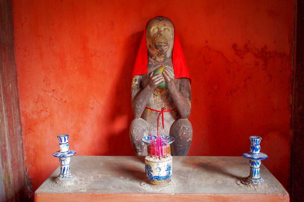 Guardian monkey statue Japanese Bridge Hoi An – A weathered guardian monkey statue draped in red cloth inside the Japanese Bridge, part of the symbolic monkey and dog statues that protect the structure.