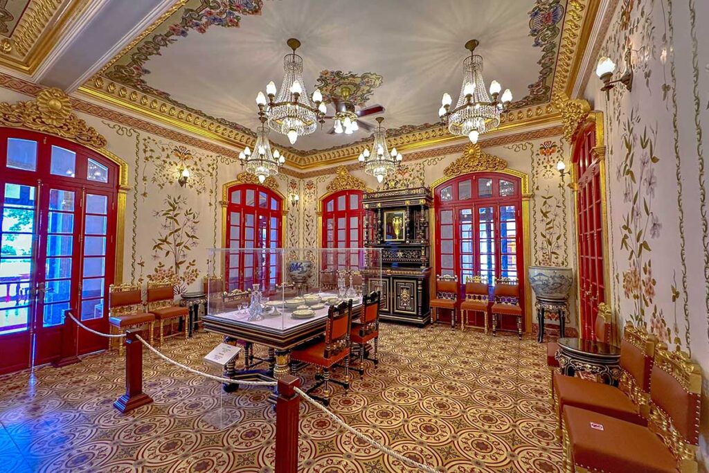 A room inside Kien Trung Palace with chandeliers, an antique dining table with porcelain tableware behind glass