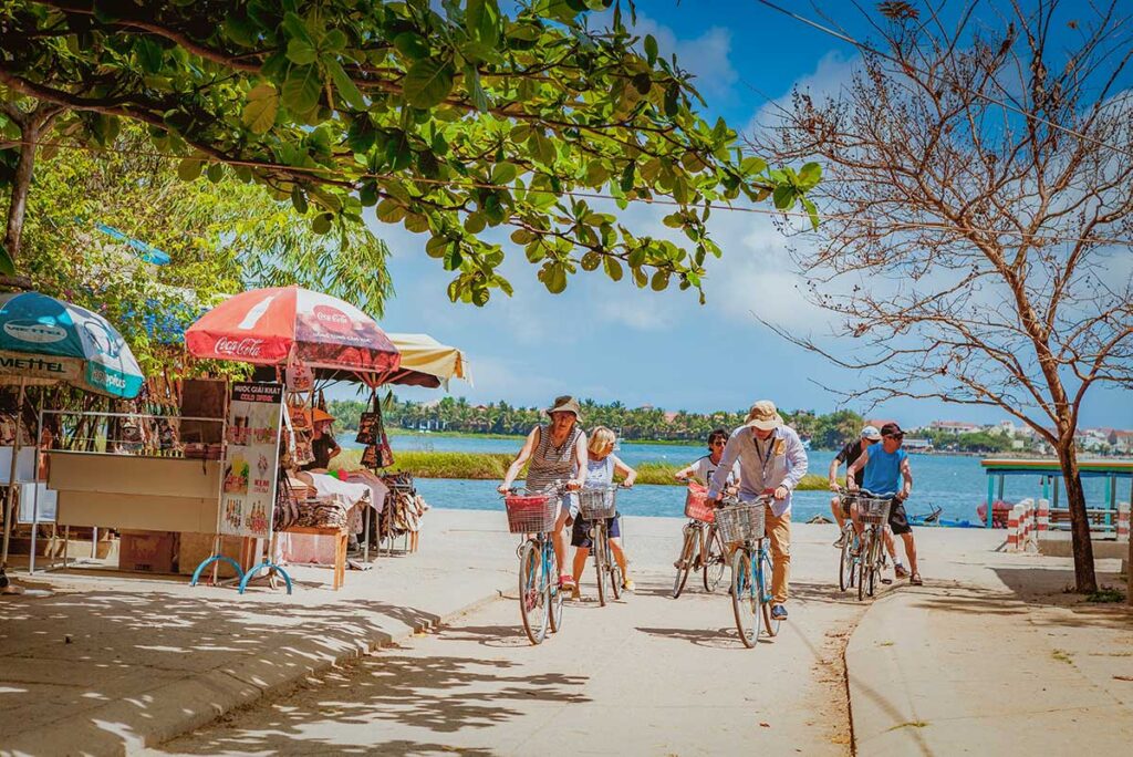 Tourists cycling past riverside stalls and craft shops in Kim Bong Carpentry Village, Cam Kim.