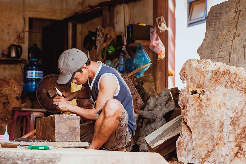 Traditional woodcarver shaping a sculpture by hand in Kim Bong Carpentry Village, Vietnam.