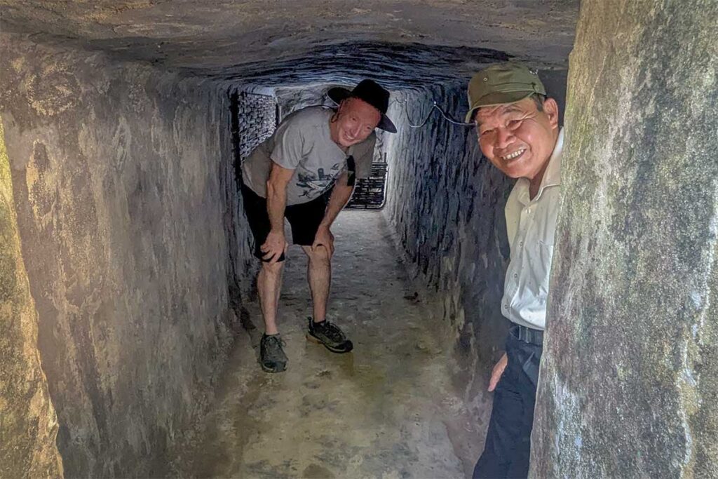 Tourists and guide exploring the low underground corridor of Ky Anh Tunnels, demonstrating the confined conditions.