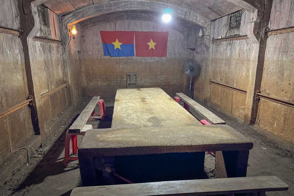 Inside Ky Anh Tunnels showing the underground meeting room with benches and national flags on the wall.