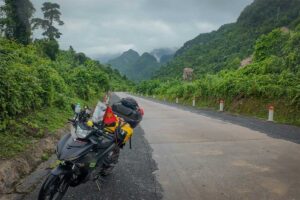 Motorbike parked along the Ho Chi Minh Highway with luggage, overlooking a misty mountain road surrounded by dense jungle