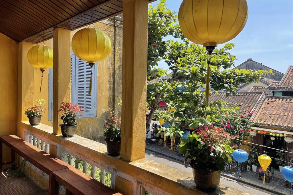 Balcony view from the Museum of Sa Huynh Culture Hoi An – Yellow lanterns and flower pots overlooking tiled rooftops and colorful lantern streets of the Old Town.