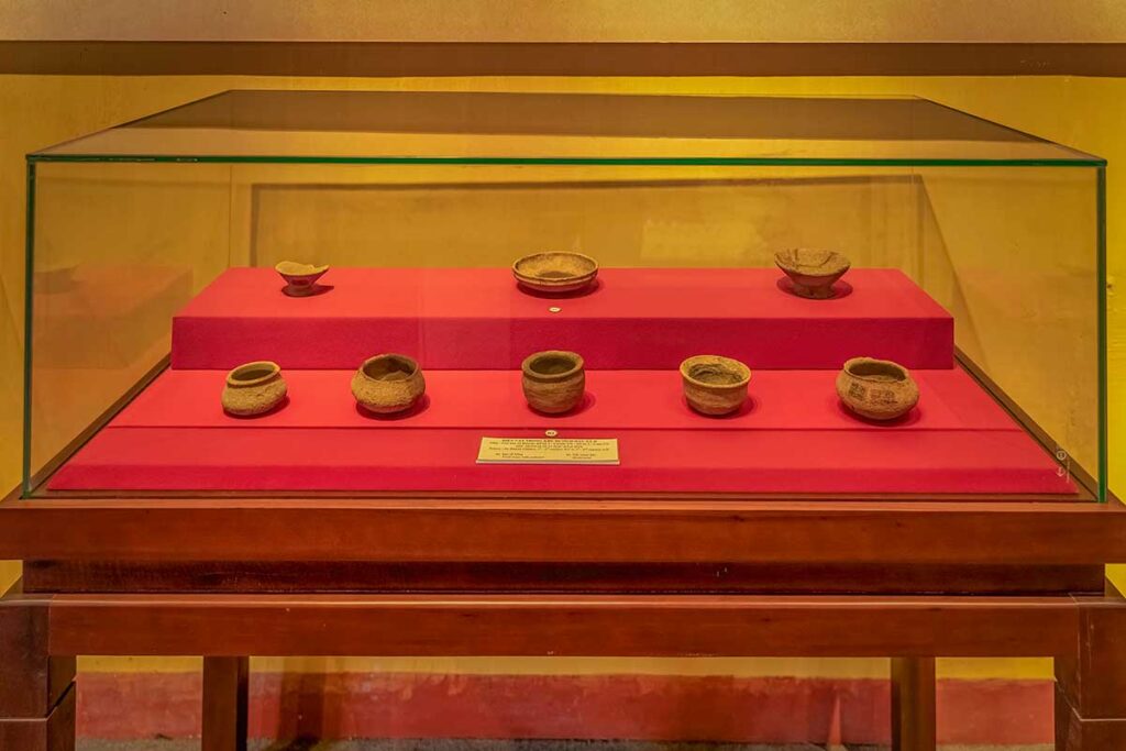 Exhibit of small Sa Huỳnh ceramic vessels in glass case at Hoi An Museum of Trade Ceramics – early archaeological finds that predate Hoi An’s trading port era.