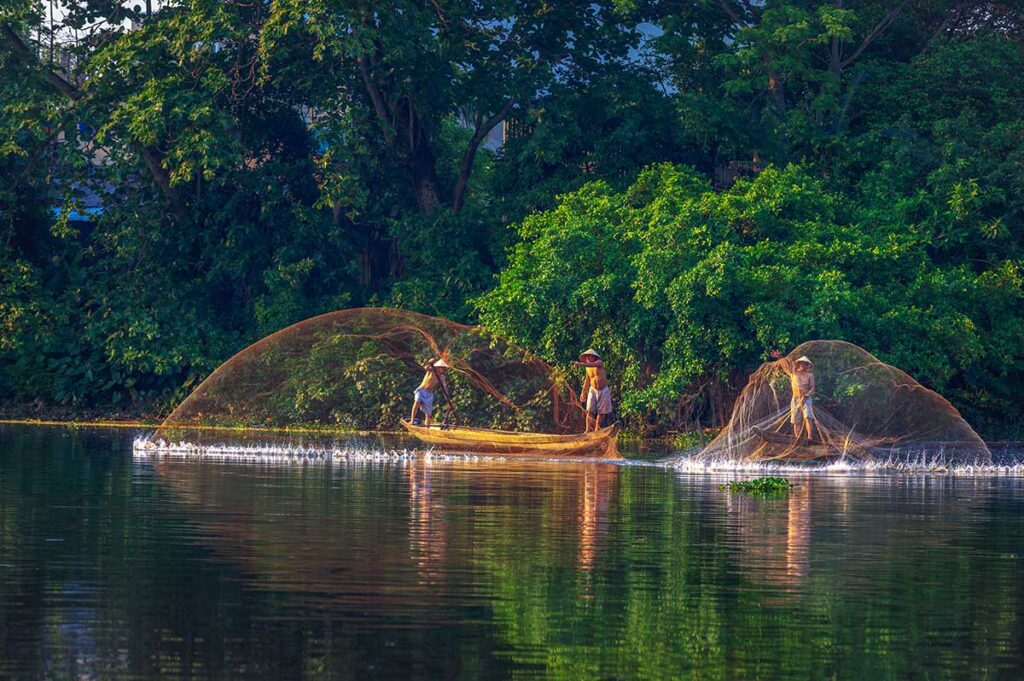 Local fisherman are throwing nets from their simple wooden boats into the Perfume River