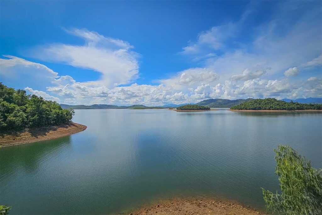 Phu Ninh Lake near Tam Ky, Quang Nam, with clear reflections, forested islands, and dramatic clouds above the water.