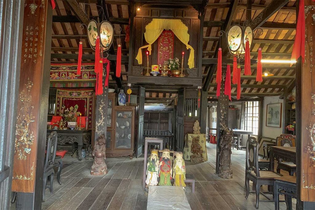 Traditional worship area on the upper floor of Phung Hung Old House in Hoi An with ancestral altar, antique chairs, and red decorative tassels.