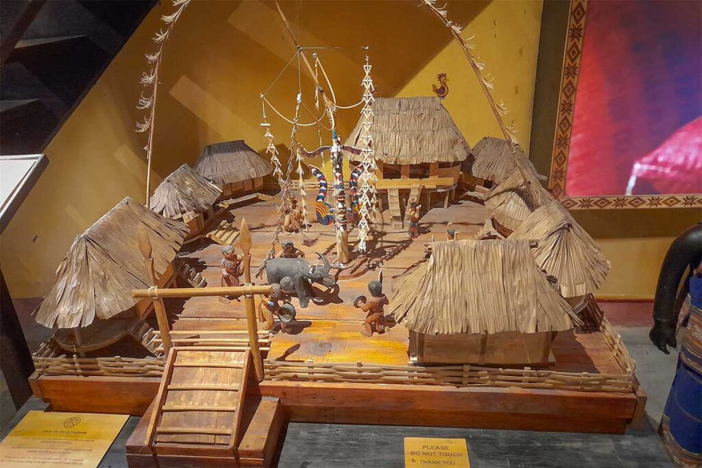 Miniature stilt house village model in Precious Heritage Museum – Detailed diorama of ethnic houses, villagers, and buffalo used for cultural education.