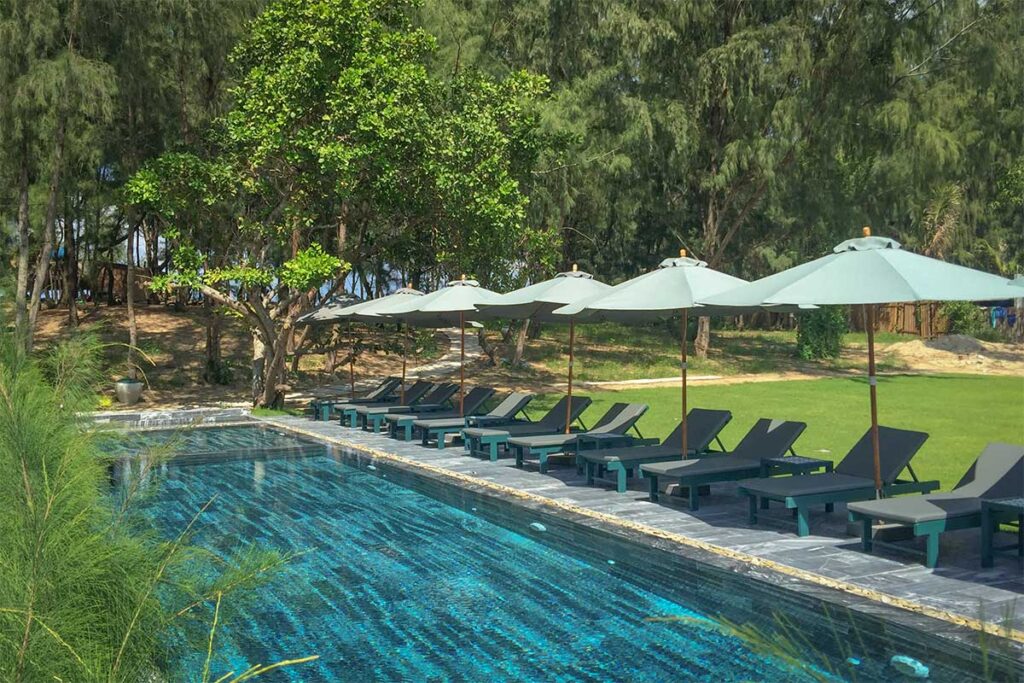 Swimming pool surrounded by sun loungers and trees at Sol An Bang Beach Resort, one of the top beachfront stays in Hoi An.