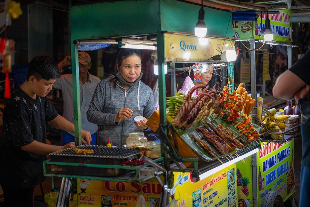 Local vendors preparing skewers and grilled snacks at the night market in Hoi An Old Town, showcasing the town’s lively street food culture.