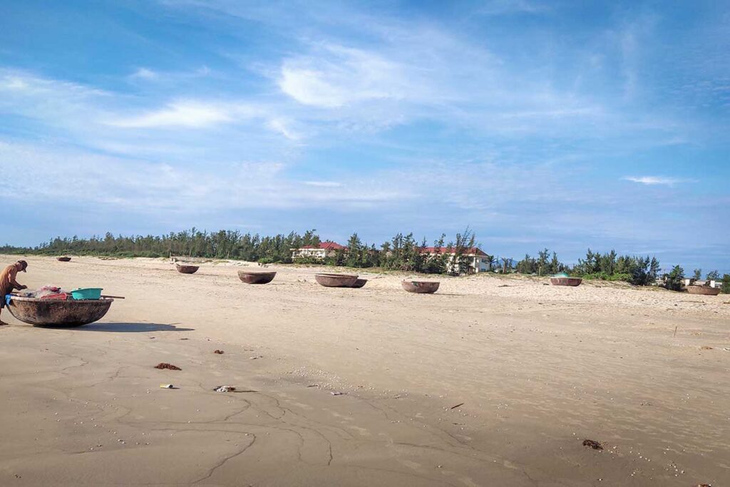 Wide sandy stretch of Tam Thanh Beach with basket boats dotting the shoreline, offering a glimpse into authentic fishing culture near Hoi An.