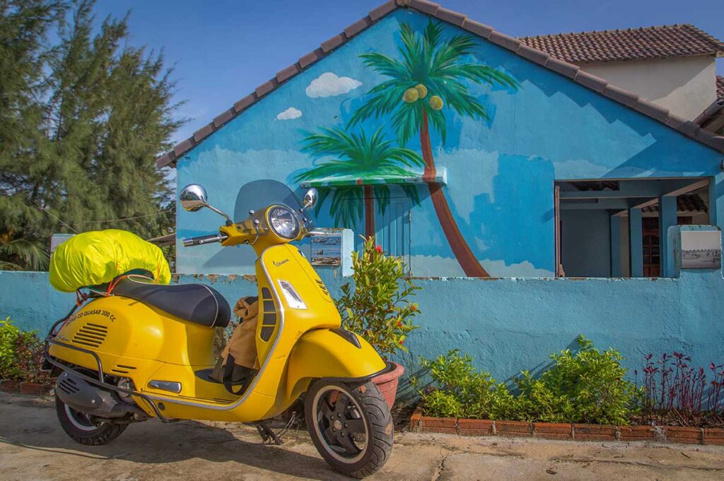 Village house painted with bright blue walls and coconut tree murals in Tam Thanh Mural Village.