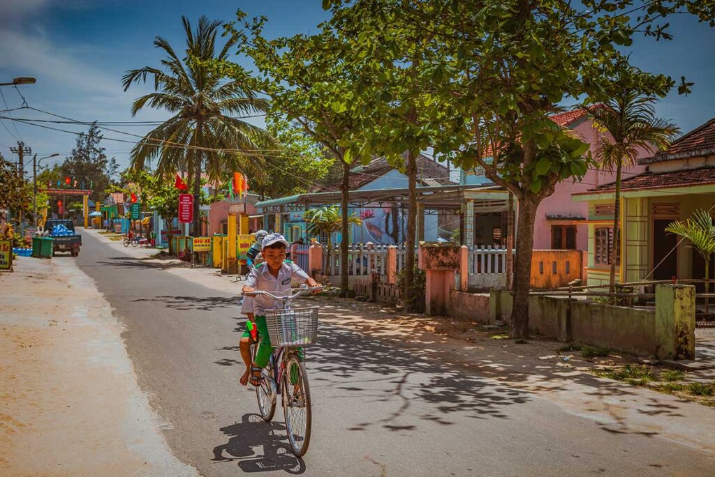 Local children cycling past painted houses in Tam Thanh Mural Village, Quang Nam Province.