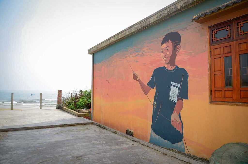 Colorful mural of a fisherman boy flying a kite on a village wall in Tam Thanh Mural Village, Quang Nam.