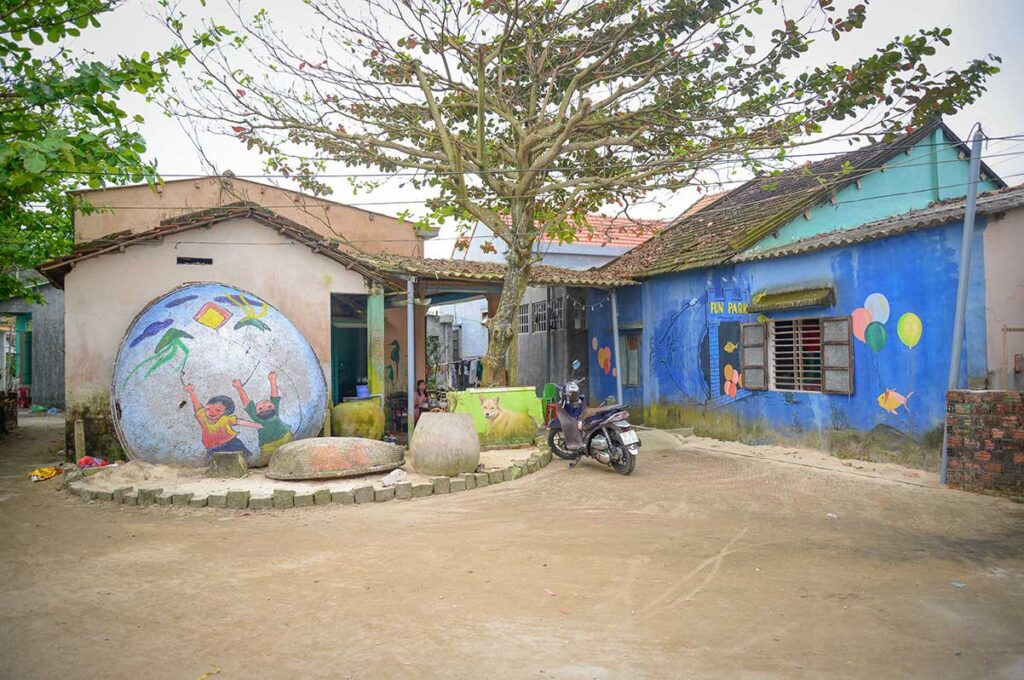 Street corner in Tam Thanh Mural Village with playful murals of balloons and sea life on old houses.