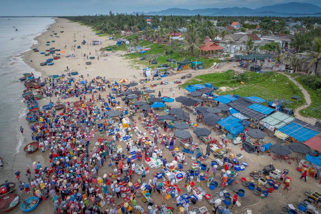 Close-up of seafood baskets filled with shrimp and fish, surrounded by busy traders at Tam Tien Beach in central Vietnam.