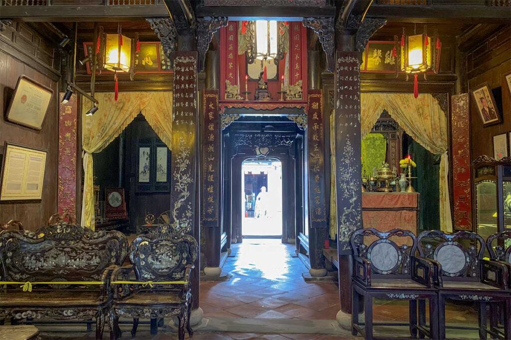 Ornate interior of Tan Ky Old House in Hoi An with carved wooden pillars, ancestral altar, antique furniture, and decorative lanterns.