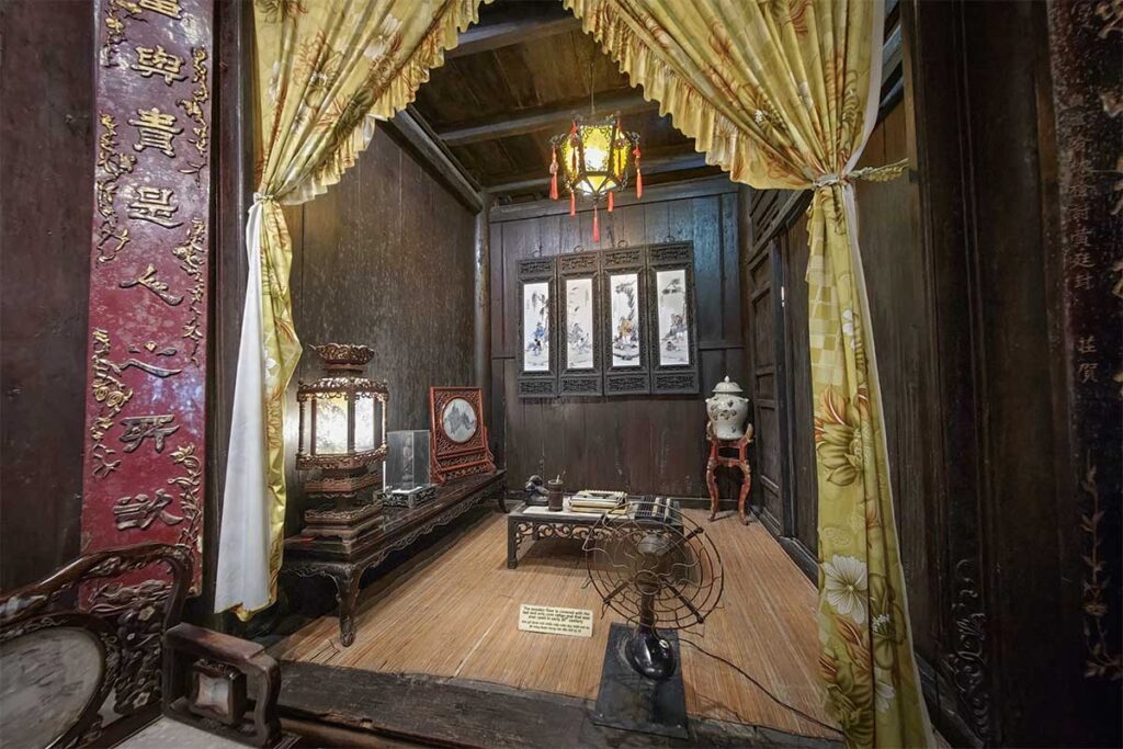 Traditional family room inside Tan Ky Old House in Hoi An, featuring lacquered furniture, ceramic jars, vintage fan, and painted calligraphy panels
