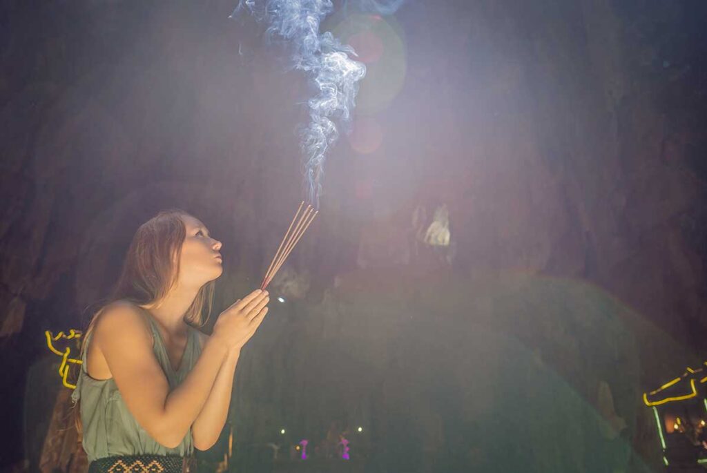 Traveler lighting incense inside a dimly lit pagoda, capturing the peaceful atmosphere of temples in Hoi An and the local spiritual traditions that continue today.