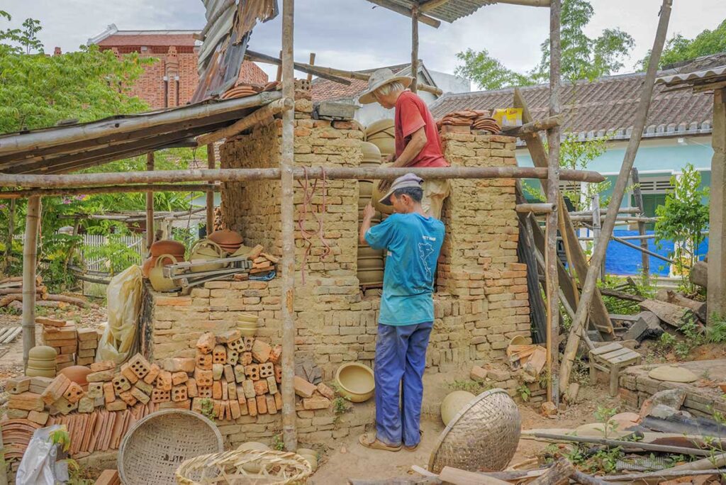 Two potters working with a traditional brick kiln at Thanh Ha Pottery Village, preserving ancient ceramic techniques