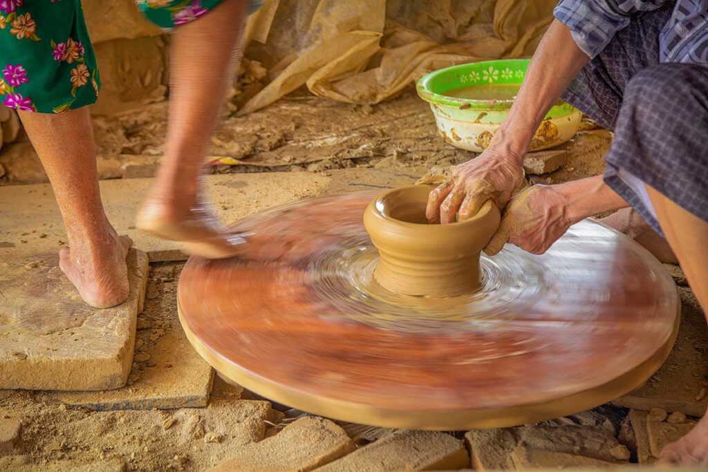 Potter shaping clay on traditional foot-powered wheel – Close-up of a craftsman molding clay while another spins the wheel with their foot.