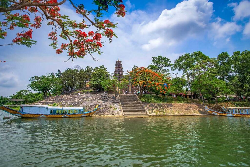 The stupa tower of Thien Mu Pagoda seen from Perfume River and a dragon boat docked below the hill