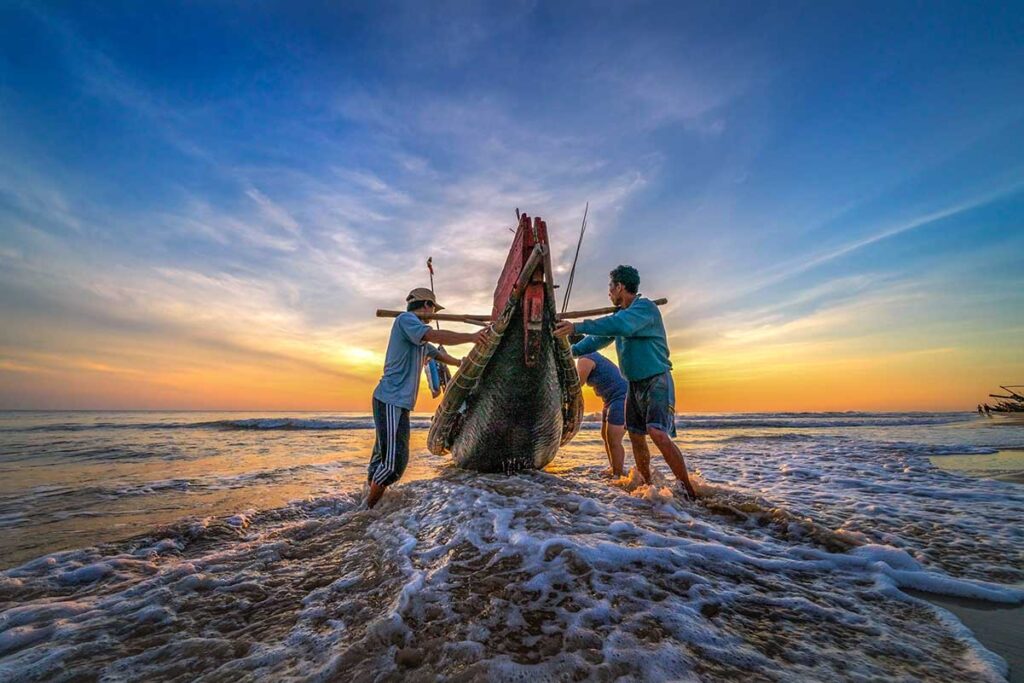 Two fishermen pushing their wooden fishing boat from Thuan An Beach into the water