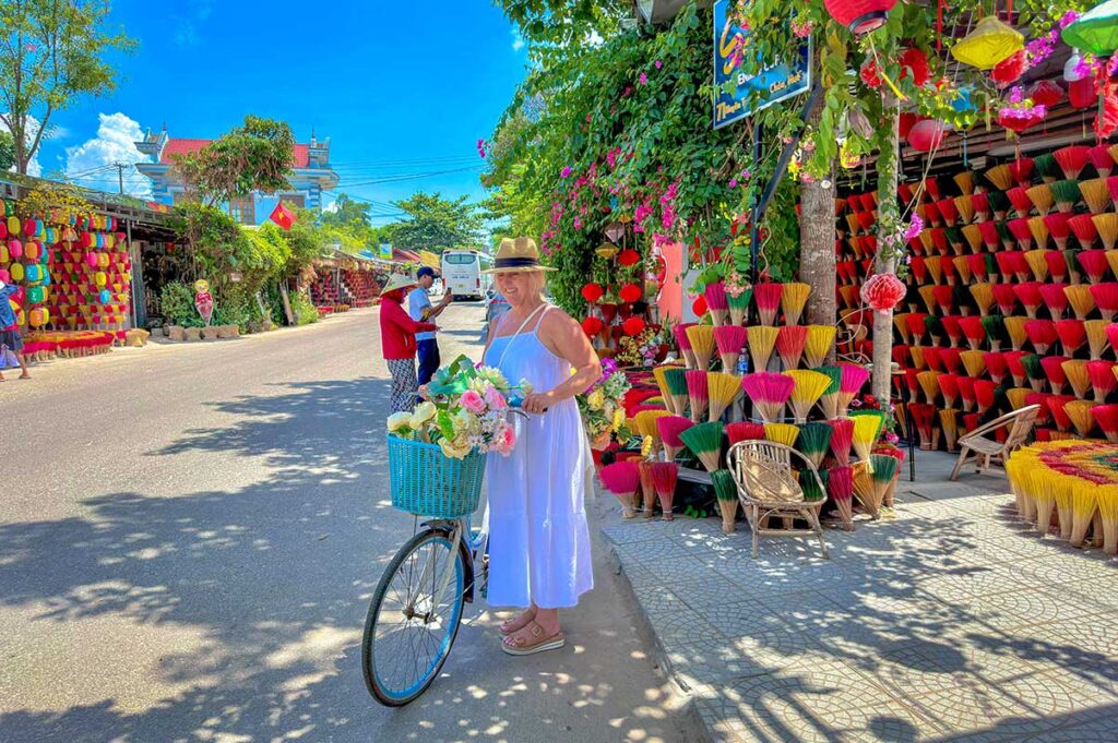 A foreign traveller is sitting on her bicycle with in the background an incense store in Tuy Xuan Village