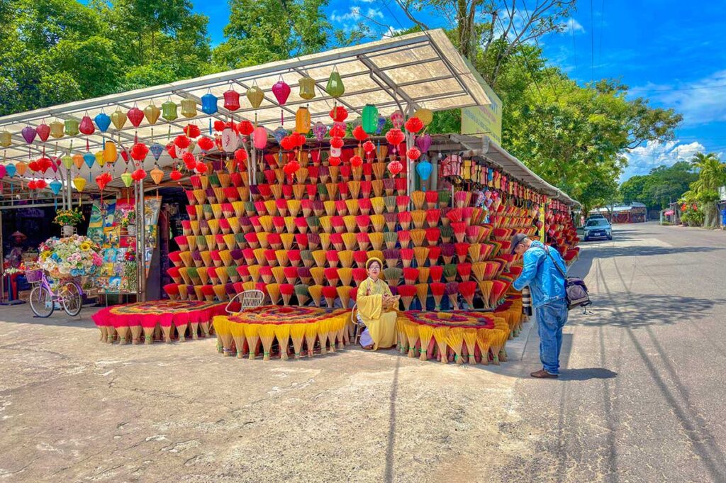 A girl is doing a photoshoot with photographer with in her background a wall of incense at Thuy Xuan Incense VIllage